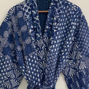 May include: A blue and white patterned robe with a tie closure. The robe features various geometric and floral designs in shades of blue and white. The robe is made of a soft, quilted fabric.