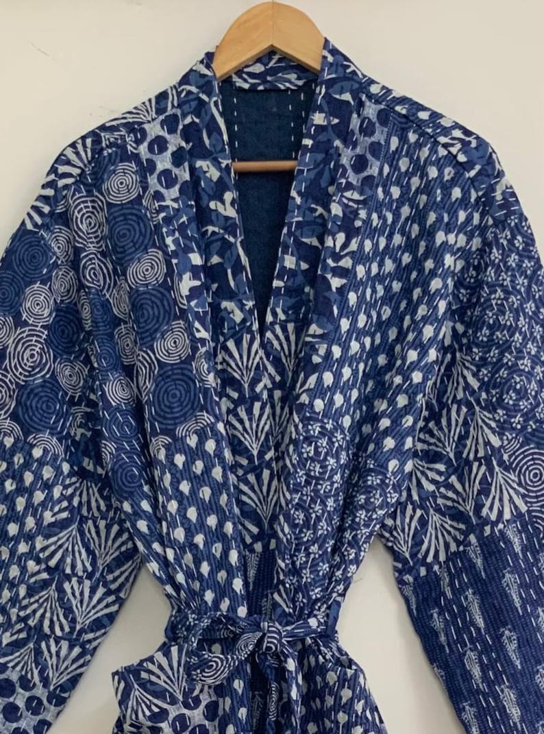 May include: A blue and white patterned robe with a tie closure. The robe features various geometric and floral designs in shades of blue and white. The robe is made of a soft, quilted fabric.