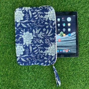 May include: A navy blue tablet case with a light blue floral design and a matching wrist strap. The case has a white zip. The tablet is partially visible, showing the home screen.