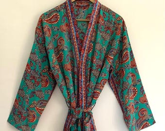 May include: A teal paisley patterned robe with long sleeves, hanging on a wooden hanger. The robe features a vibrant design with red, blue, and white accents. The robe is tied at the waist with a matching fabric belt.