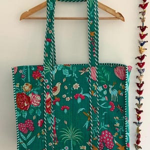 May include: A green tote bag with a floral print and white trim. The bag has a long handle and is made of cotton.