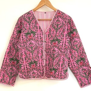 May include: A pink quilted jacket with a floral print and a white and pink striped lining. The jacket has a button closure and long sleeves.