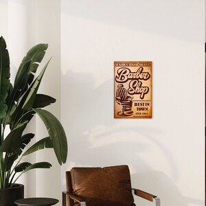 Peut inclure: Une enseigne de style vintage pour un salon de coiffure. L'enseigne est brune avec un aspect délavé et présente un fauteuil de barbier à rayures. Le texte sur l'enseigne indique "Haircut and Shave Barber Shop Best in Town Est'd 2014".