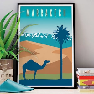 Op de afbeelding: Een vintage reisposter in de kleuren blauw, groen en bruin. De poster toont een kameel silhouet op de voorgrond, een palmboom en een bergketen op de achtergrond. De tekst "MARRAKECH" staat bovenaan de poster.