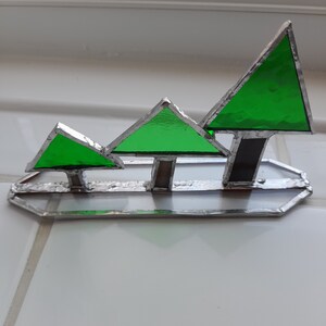 May include: Three green stained glass trees of different sizes on a silver base. The trees are arranged in a row from smallest to largest.