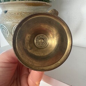 May include: Brass candle holder with a round base and a decorative design. The base is smooth and shiny.