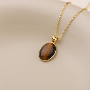 May include: A gold chain necklace with a brown oval pendant featuring a tiger's eye stone.