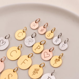Puede incluir: Surtido de dijes de metal dorado, plateado y oro rosa con diversas grabaciones de letras y diseños. Los dijes son redondos y tienen un agujero en la parte superior para sujetarlos a un collar o pulsera.