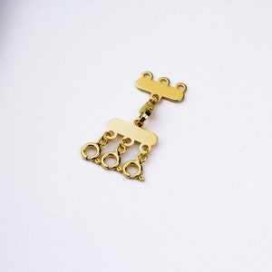 May include: Gold-toned metal jewelry connector with multiple loops. The connector has a rectangular shape with a row of four loops on one side and a row of three loops on the other side.