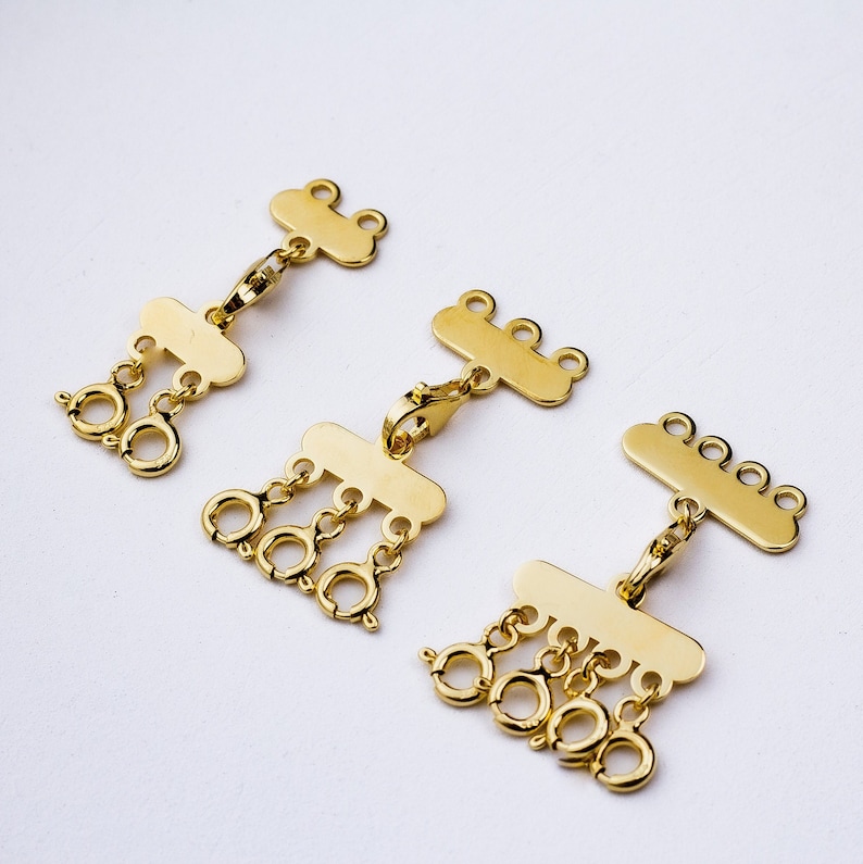 May include: Three gold-tone metal jewelry clasps with multiple loops. Each clasp has a flat rectangular shape with a row of loops on one side.