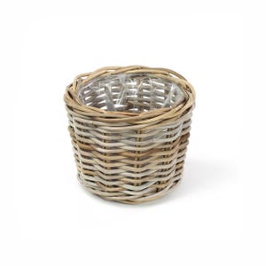 May include: A round, woven wicker basket with a natural light brown finish. The basket features a sturdy, braided rim and a clear plastic liner fitted inside the interior, providing a functional container for various household items or plants.