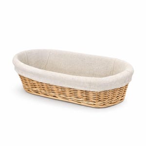 May include: An oval wicker basket with a fabric lining. The basket is made from woven, light brown wicker and has a smooth, curved shape. The fabric lining is a neutral beige colour, providing a soft contrast to the wicker.