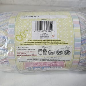 K&ouml;nnte beinhalten: Nahaufnahme eines Garnetiketts mit dem Text "LOT 1693 0612" und "BABY OMBRE" in einem hellblauen und wei&szlig;en Farbschema. Das Etikett enth&auml;lt auch Anweisungen zum Starten einer Garnkugel und Waschanweisungen.