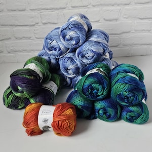 May include: A collection of colorful yarn skeins in shades of blue, green, and orange. The yarn is arranged in a pile, with the orange skein in the foreground. The yarn has a variegated color pattern, with labels visible on some skeins.