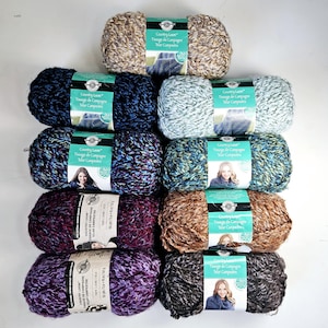 Peut inclure: Dix écheveaux de fil Country Loom disposés en deux colonnes. Le fil présente diverses fibres texturées multicolores dans des tons de beige, bleu marine, bleu clair, sarcelle, violet, marron et gris anthracite, chacun avec une étiquette en papier.