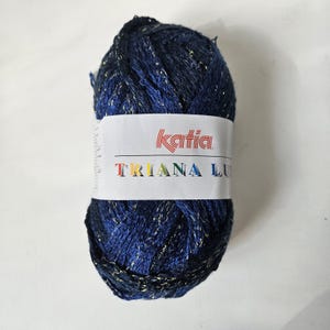 May include: A ball of Katia Triana Lux yarn in shades of navy blue with gold metallic threads. The yarn is wrapped with a white label featuring the Katia logo and the yarn name. Ideal for knitting and crochet projects.