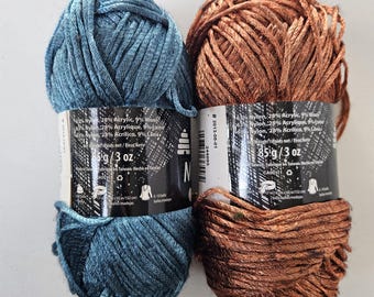 May include: Two skeins of yarn, one in a deep teal blue and one in a metallic copper brown. Each skein features a black paper label with white text stating 63% nylon, 28% acrylic, 9% wool, and a net weight of 85 grams or 3 ounces per skein.