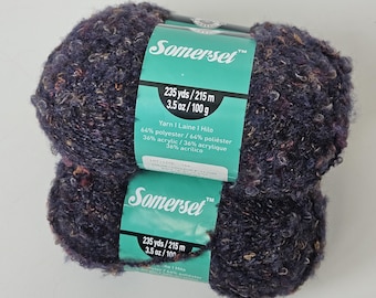 May include: Two skeins of dark purple textured yarn with multi-colored flecks. The teal paper label reads Somerset, 235 yds, 3.5 oz, 64% polyester, and 36% acrylic. The yarn has a fuzzy, looped appearance with visible specks of orange and white.