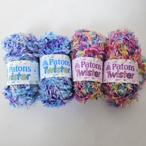 May include: Four skeins of Patons Twister yarn in shades of blue, purple, pink, and yellow. The yarn has a fluffy, textured appearance. Each skein is labelled with the brand name and product details.