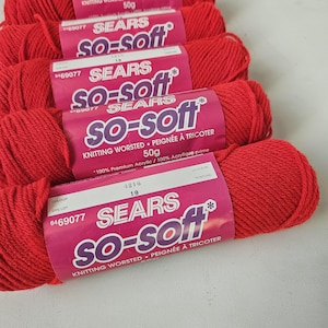 May include: A collection of red knitting yarn skeins, each with a pink and white label. The labels display "SEARS SO-SOFT" and "KNITTING WORSTED". Each skein contains 50g of yarn, made from 100% acrylic.