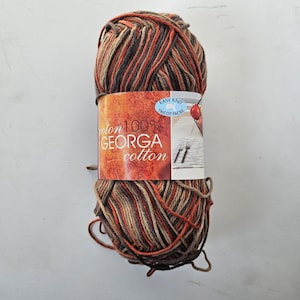 May include: A ball of multi-colored yarn with shades of brown, orange, and tan. The yarn is wrapped with a label that reads "GEORGA cotton 100%" and "EASY KNIT". The yarn is suitable for knitting and crochet projects.