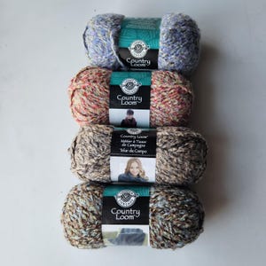 May include: Four skeins of Loops & Threads Country Loom yarn stacked vertically. The top skein is blue and purple, the second is red and orange, the third is brown and tan, and the bottom is blue, brown, and tan. Each has a paper label.