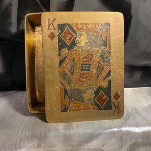 May include: A rectangular brass box with a lid featuring an engraved King of Diamonds playing card design. The lid displays the letter K and a diamond symbol in the corners, with a detailed illustration of a king in gold, black, and red tones.
