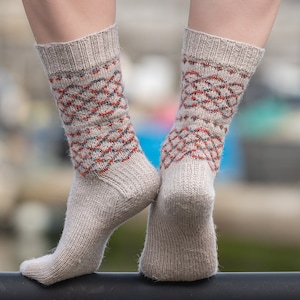 May include: A pair of beige socks with a geometric pattern in red, blue, and gray. The socks are made of a soft, knitted fabric and are shown on a person's feet.