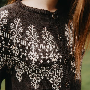 以下が含まれることがあります： 白の幾何学模様が施された濃い茶色のカーディガン。ボタンダウンセーターはクルーネックと長袖が特徴です。セーターは柔らかいニット素材で作られています。