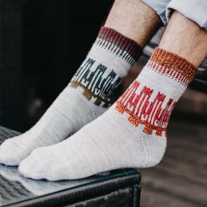 May include: A pair of gray socks with colorful geometric patterns. The socks have a red, orange, and blue pattern on one sock and a red, orange, and green pattern on the other sock.