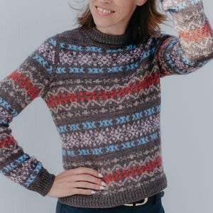 Può includere: Un maglione in maglia a maniche lunghe con base marrone scuro e un motivo fair isle ripetuto in azzurro, lavanda e arancione brillante. Il maglione presenta un girocollo a coste, polsini a coste e un orlo a coste, con una linea aderente.