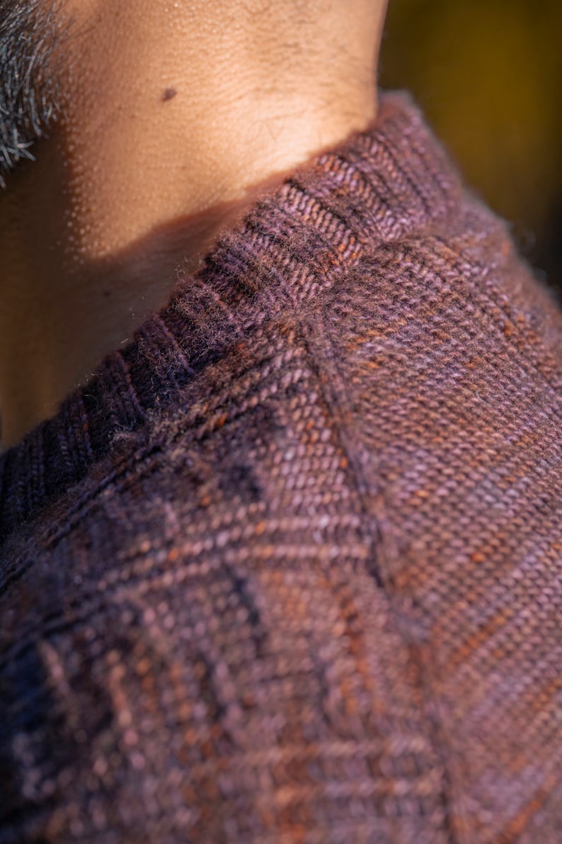 May include: Close-up of a brown and purple knitted sweater with a textured pattern. The sweater has a ribbed collar.