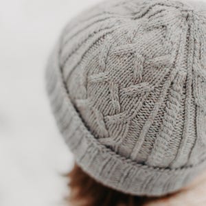 Puede incluir: Un gorro de punto gris con un patrón de trenza.