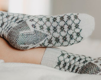May include: A pair of white socks with a green and brown diamond pattern. The socks are made of a soft, knitted fabric.