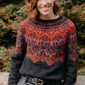 May include: A long-sleeved knit jumper featuring a dark charcoal base with a vibrant yoke pattern in shades of bright orange, deep red, and magenta. The jumper has a round neckline and a textured, fuzzy wool-like appearance throughout the garment.