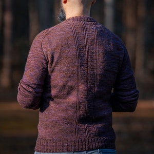 May include: A person wearing a purple and brown sweater with a ribbed texture. The sweater has a crew neck and long sleeves.