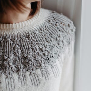 May include: A white knitted jumper with a grey cable knit design around the neckline.