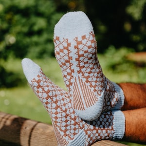 May include: A pair of light blue and brown knit socks featuring a repeating geometric diamond pattern. The socks have a solid light blue toe and heel section, with a ribbed cuff and a textured knit construction throughout the foot and ankle area.