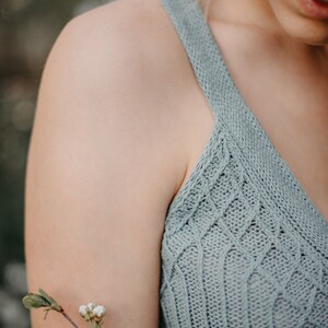 Peut inclure: Gros plan sur l'&eacute;paule et le bras d'une femme portant un d&eacute;bardeur en tricot bleu clair. Une petite branche de fleurs blanches repose sur son bras.