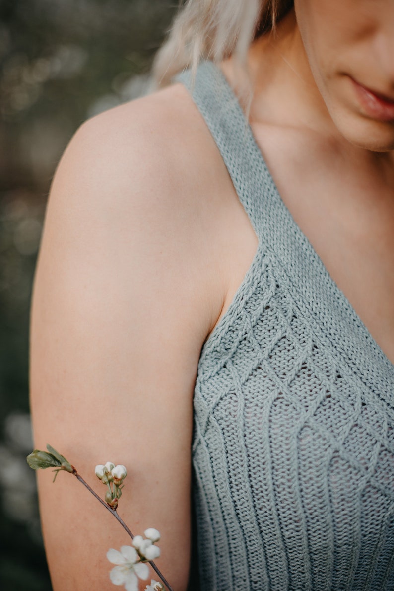 Peut inclure: Gros plan sur l'&eacute;paule et le bras d'une femme portant un d&eacute;bardeur en tricot bleu clair. Une petite branche de fleurs blanches repose sur son bras.