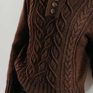 May include: A brown cable knit sweater with a button-up collar. The sweater has a textured pattern and is made of a soft, warm material.
