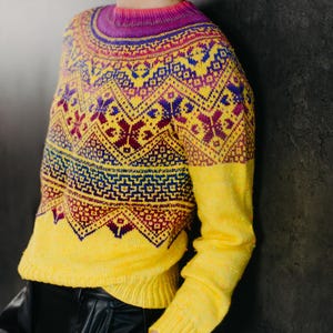Op de afbeelding: Een gele trui met een kleurrijk geometrisch patroon. De trui heeft een ronde hals en lange mouwen.