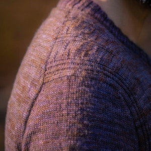 May include: Close-up of a brown knitted sweater with a textured pattern. The sweater is made of a soft, comfortable material.