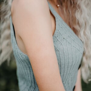 Peut inclure: Gros plan sur le bras d'une femme portant un haut sans manches en tricot bleu clair. Le haut a une texture c&ocirc;tel&eacute;e et un motif d&eacute;licat.