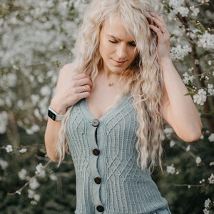 Peut inclure: Une femme aux longs cheveux blonds portant un d&eacute;bardeur en tricot bleu clair avec des boutons en bois et un short en jean. Elle se tient devant un arbre &agrave; fleurs blanches.