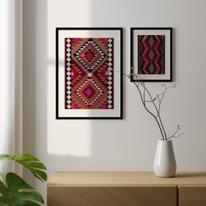 May include: Two framed prints of colorful geometric patterns in shades of red, orange, pink, blue, and black. The prints are hanging on a white wall above a wooden shelf.