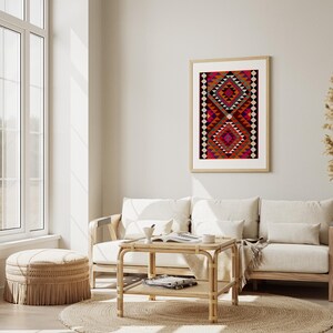 May include: A white couch with pillows sits in a living room with a wooden coffee table and a woven ottoman. A framed print of a colorful geometric pattern hangs on the wall.