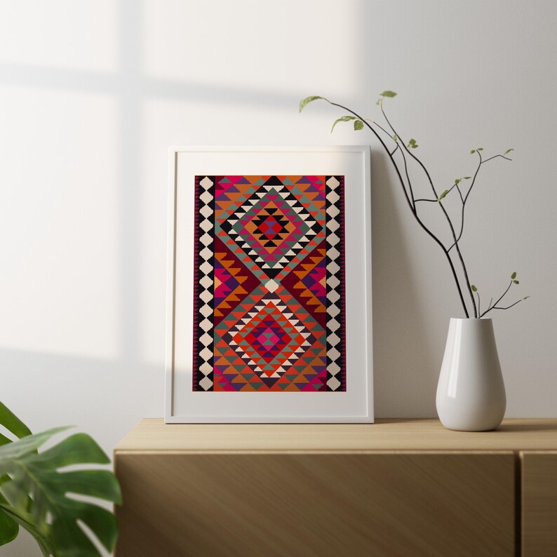 May include: A framed print of a colorful geometric rug with a repeating pattern of diamonds and triangles in shades of red, orange, pink, green, and black.