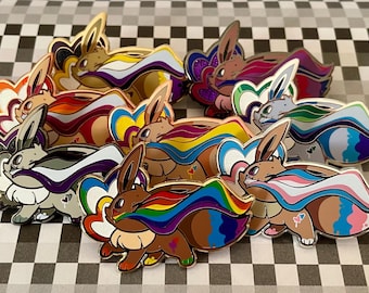May include: A set of ten enamel pins featuring a cartoon character with different colored pride flags. The character is brown with a long, pointed snout and large ears. The flags are rainbow, transgender, bisexual, lesbian, pansexual, asexual, genderfluid, non-binary, intersex, and aromantic.