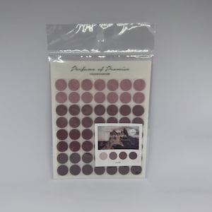 Könnte beinhalten: Ein Bogen mit runden rosa und violetten Aufklebern mit einem Farbverlauf. Die Aufkleber sind in einer durchsichtigen Plastiktüte verpackt. Die Verpackung enthält den Text "Perfume of Promise" und "Colour & Nature".